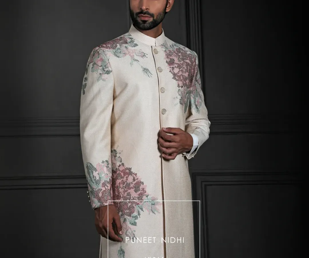 An ivory silk Achkan where artistry blooms. The clean, straight cut is a canvas for blush-pink and sage-green floral embroidery that sweeps across the shoulders and cuffs, a testament to modern elegance and timeless craftsmanship.