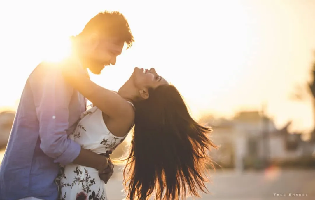 Pure joy captured during a golden hour sunset. The couple shares a spontaneous, laughing moment, with the warm light creating a beautiful, romantic flare that highlights their connection.