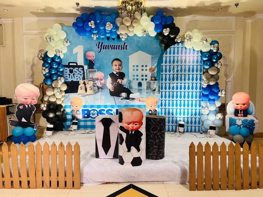 A full stage setup for a classic Boss Baby first birthday party. I used a custom-printed backdrop with the child's name, multiple character cutouts, a themed balloon arch in blue, black, and silver, and a small picket fence to complete the look.