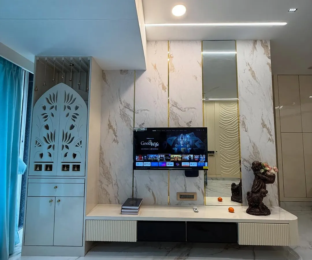 A glimpse of a finished living room in Mumbai, integrating a custom TV unit with marble-finish panels and a beautifully crafted pooja mandir with jaali work. The design balances modern aesthetics with traditional values.