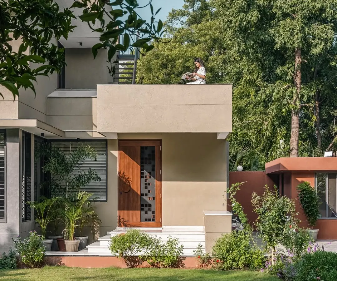 **The Glow House, Ahmedabad:** The exterior of this home is designed to capture the magic of light throughout the day. Tucked into a lush garden, the structure's clean lines and deep porch create a perfect spot for quiet moments, where the architecture itself becomes a frame for the surrounding nature.