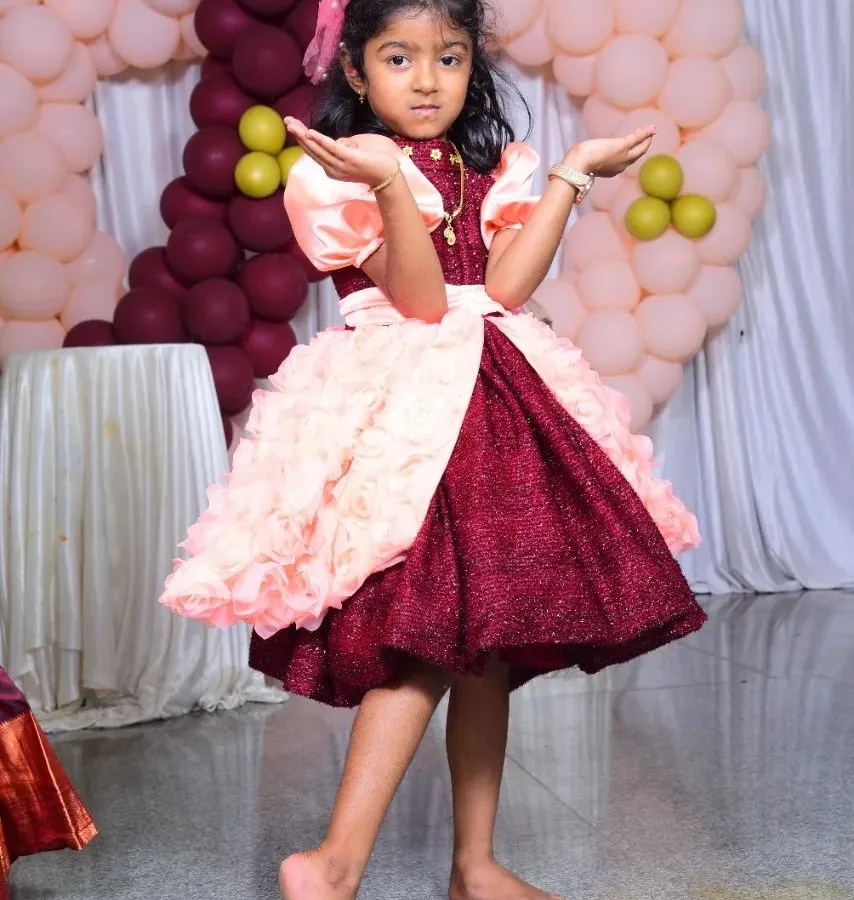 Look at this little one striking a pose! I designed this custom birthday frock with a sparkling maroon skirt and fluffy pink floral details just for her special day. Seeing her so happy and confident is the best reward.