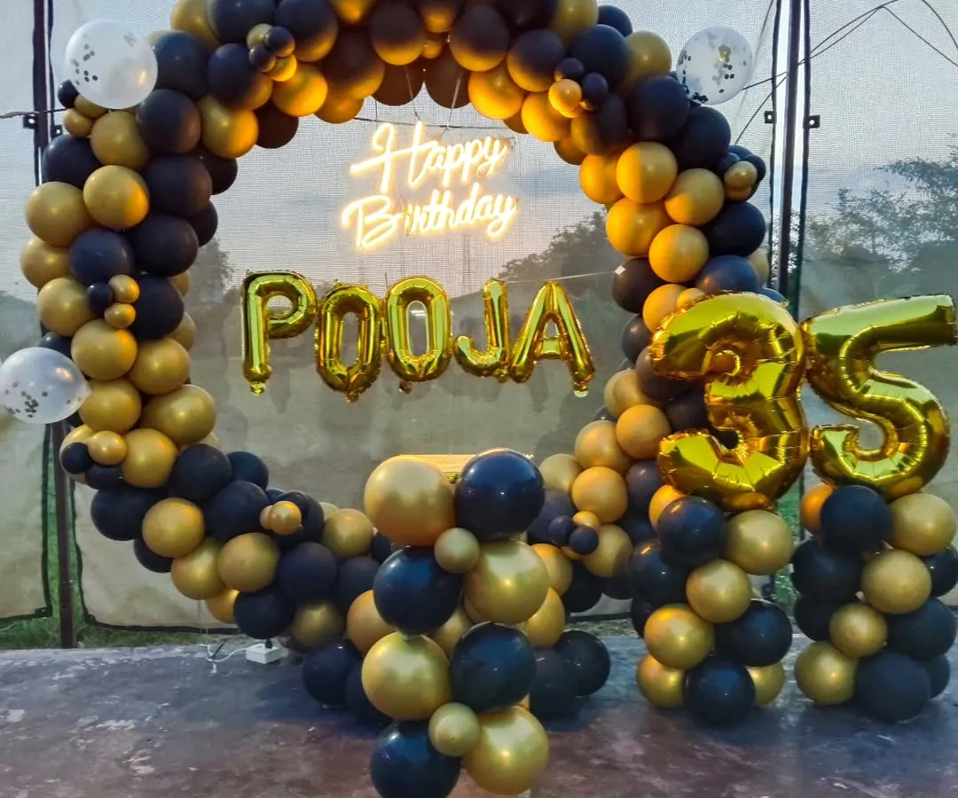 I design sophisticated decorations for milestone birthdays, like this stylish setup for a 35th celebration. It features a full ring backdrop covered in classic black and metallic gold balloons. To make it personal, I add large gold foil balloons for the name and age, along with a bright neon sign.
