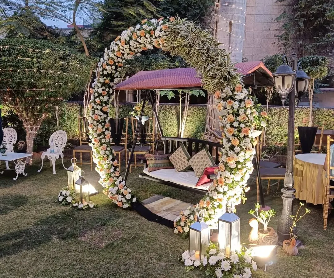 For this garden party in Gurugram, I created a romantic floral swing setup. The circular arch is covered in fresh white and peach roses, making it a perfect photo spot for guests. The lanterns and classic lamp post add a warm, magical glow to the evening.