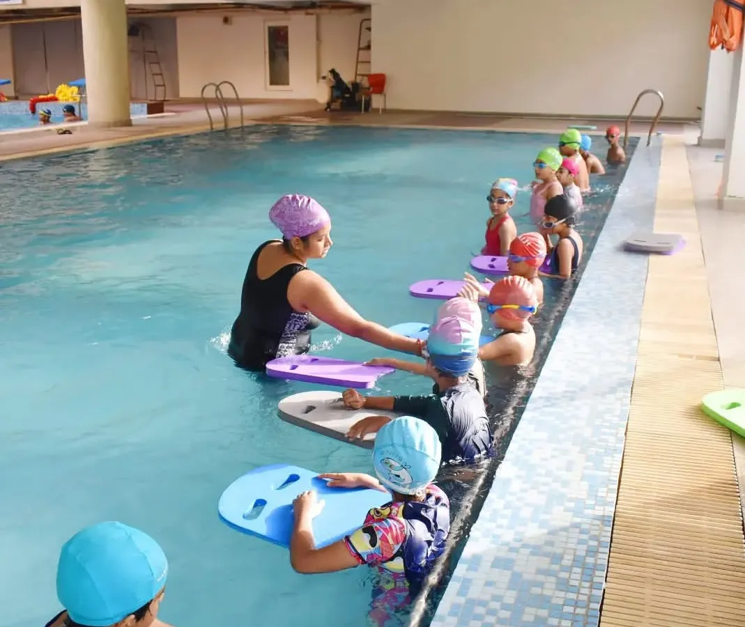 I believe in hands-on coaching, especially for young beginners. Here, our female coach guides kids through their first kicking exercises with kickboards in our Gurgaon pool.