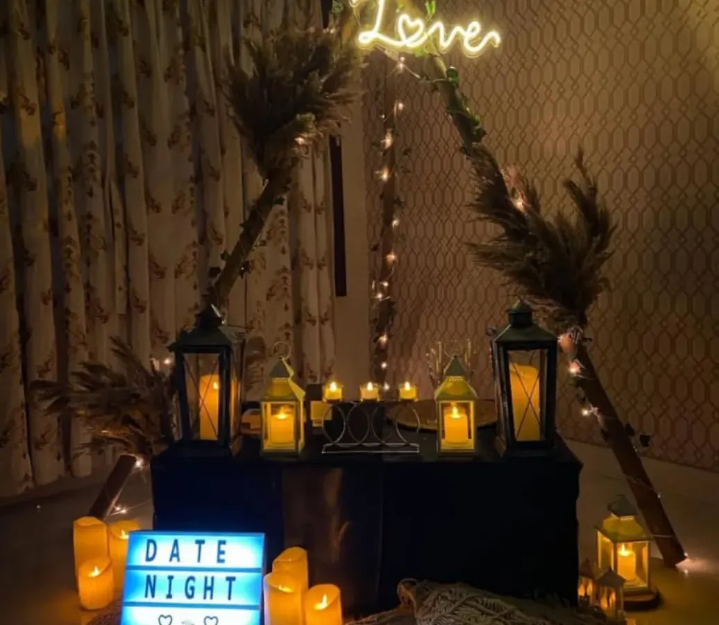 For a cozy and personal evening, I created this intimate date night setting. It features a boho-style teepee frame, warm candlelight from lanterns, a custom 'Love' neon sign, and comfortable floor seating with macrame pillows, perfect for a private celebration at home.
