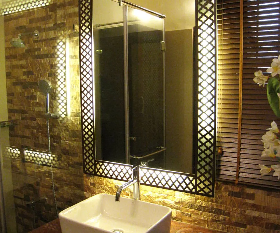 For this bathroom renovation, the focus was on creating a warm and luxurious atmosphere through texture and light. I designed a custom backlit mirror with a traditional jaali pattern frame, which becomes the centerpiece. This is set against a natural stone tile wall to add depth and character to the vanity area.