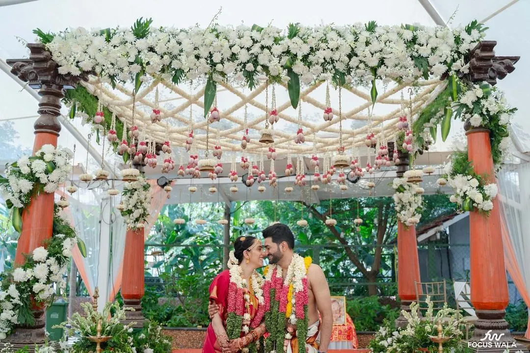 We believe in creating picture-perfect moments. Here, the couple shares a quiet moment under a custom-designed mandap, rich with fresh white orchids and traditional hanging bells, embodying the blend of intimacy and grandeur we strive for in our South Indian wedding designs.