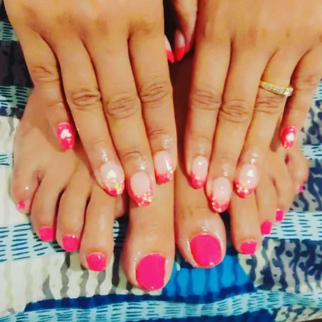I love creating a complete look with matching hands and feet. Here, I've paired a vibrant, solid hot pink pedicure with a detailed French manicure that has glitter and small heart accents for a fun, coordinated style.