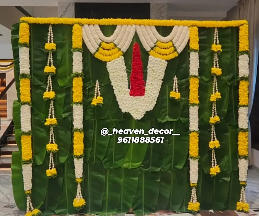 This backdrop is a tribute to South Indian tradition, crafted for a sacred ceremony. We used a full wall of fresh banana leaves, accented with garlands of jasmine and marigold, and a central floral 'Namam' to create an authentic and divine atmosphere.