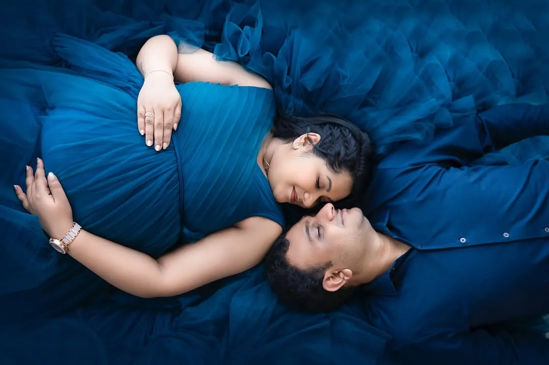 An artistic overhead shot from a maternity session, with the couple surrounded by a sea of deep blue fabric. This creative approach to pregnancy photography highlights the beauty and intimacy of this special time.