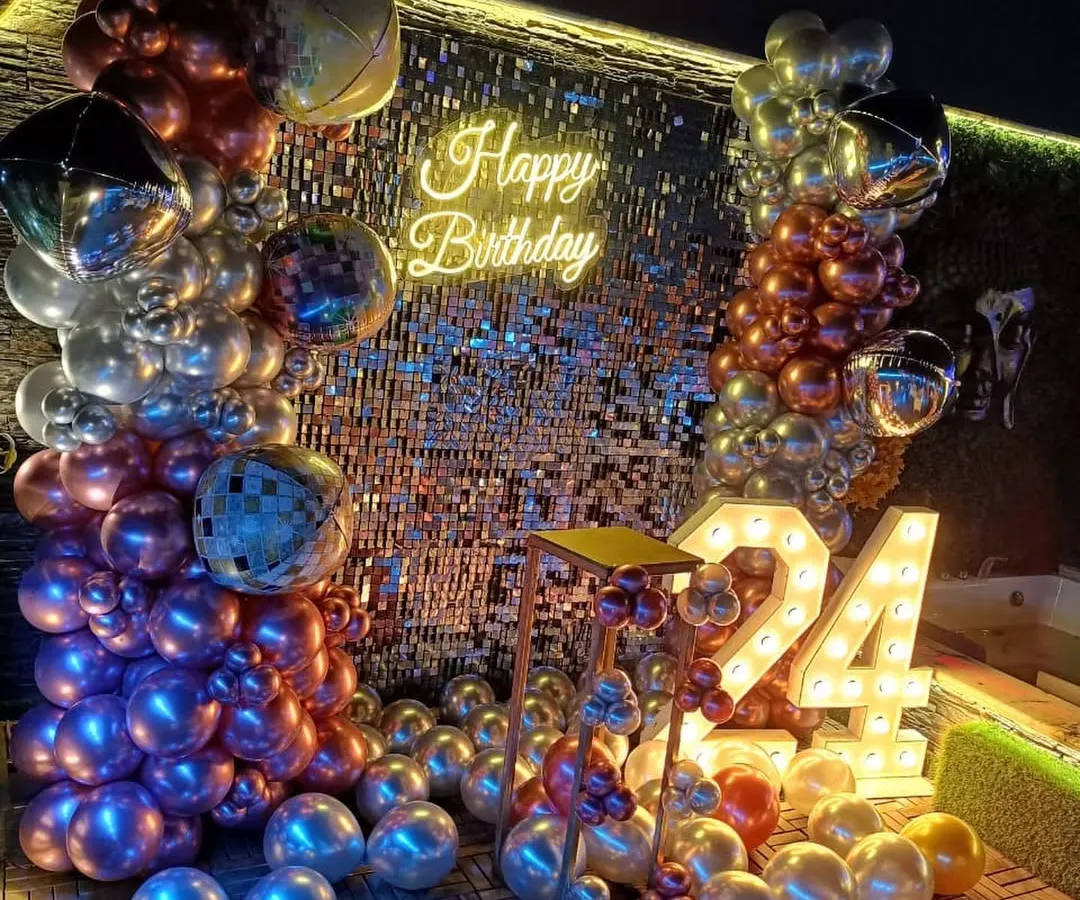 For a glamorous and high-energy celebration, I design photo backdrops like this full shimmer sequin wall. This 24th birthday setup includes large light-up marquee numbers, a 'Happy Birthday' neon sign, and a balloon garland with chrome, metallic, and disco ball accents for a party-ready look.