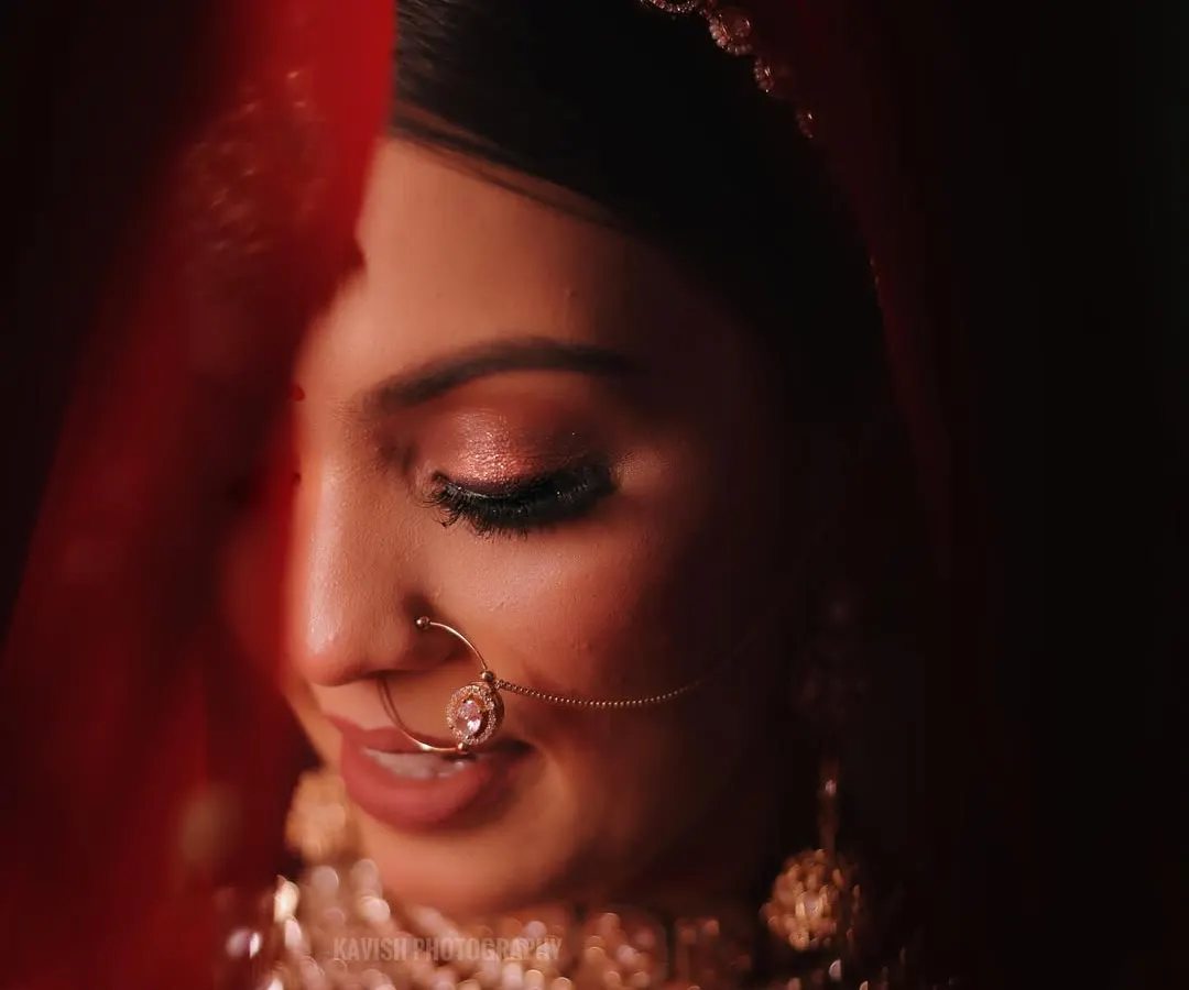 A classic bridal portrait, using the red veil to create a soft, intimate frame. This signature shot focuses on the bride's serene expression and detailed makeup.