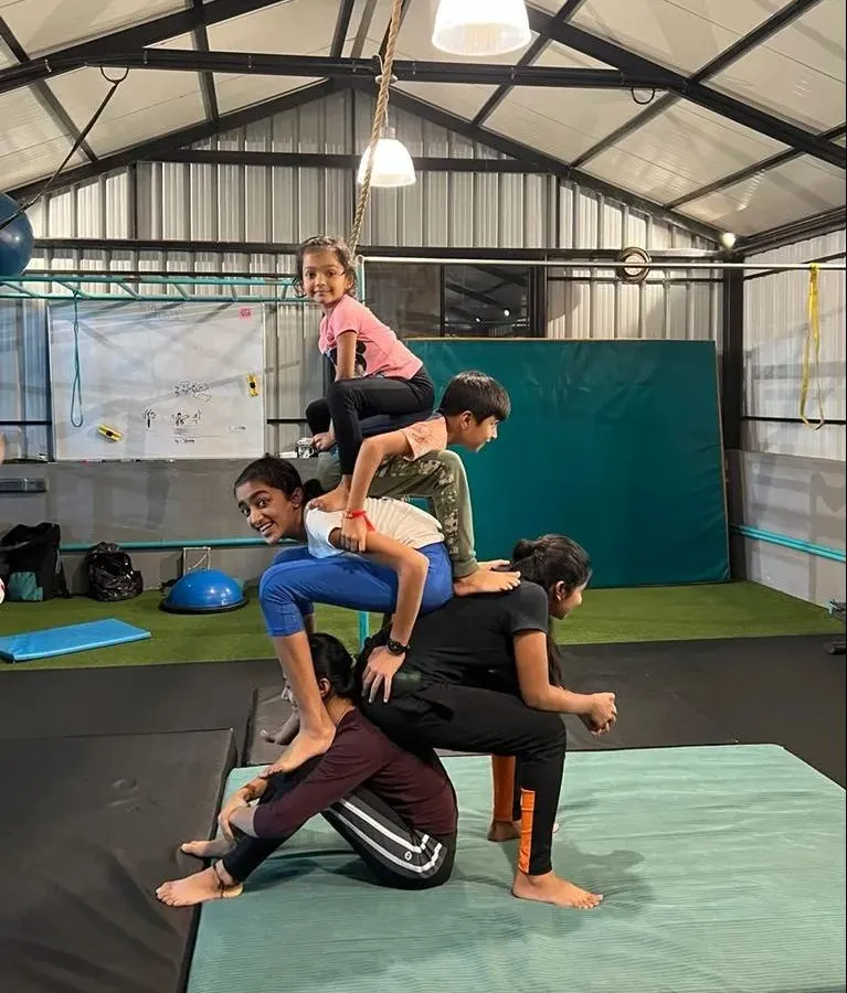 Teamwork makes everything better. Here, my students are working together to build a five-person human pyramid. This kind of partner acrobatics builds strength, balance, and trust between the kids.