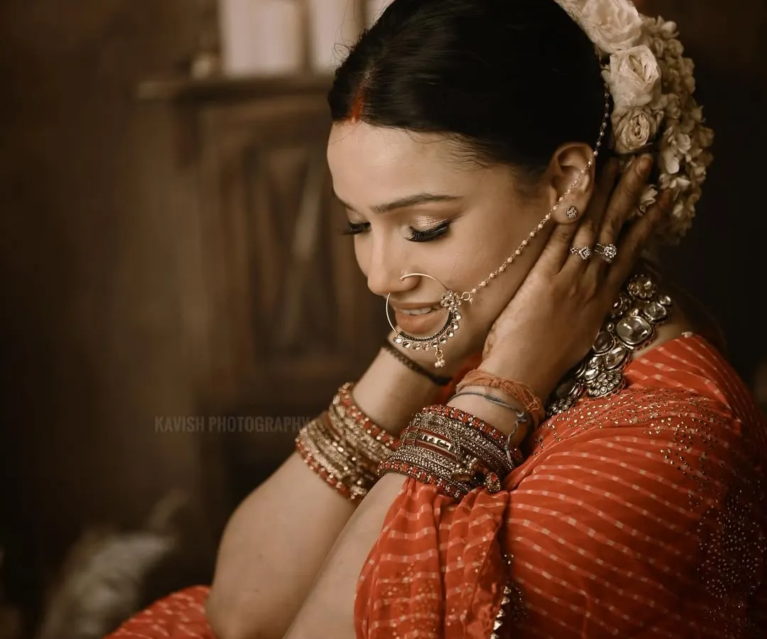 A dramatic bridal portrait using low-key lighting to create a moody and timeless feel. The focus is on the bride's quiet elegance, traditional jewelry, and the rich textures of her attire in a studio setting.
