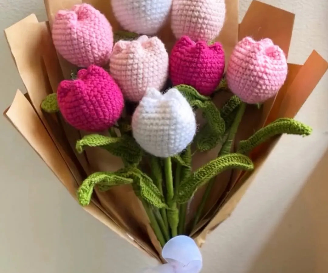 A bouquet that lasts forever. This handcrafted crochet tulip bouquet features a mix of pink, white, and fuchsia tulips, all meticulously stitched and wrapped in brown paper with a delicate white ribbon. It's a timeless gift of love.