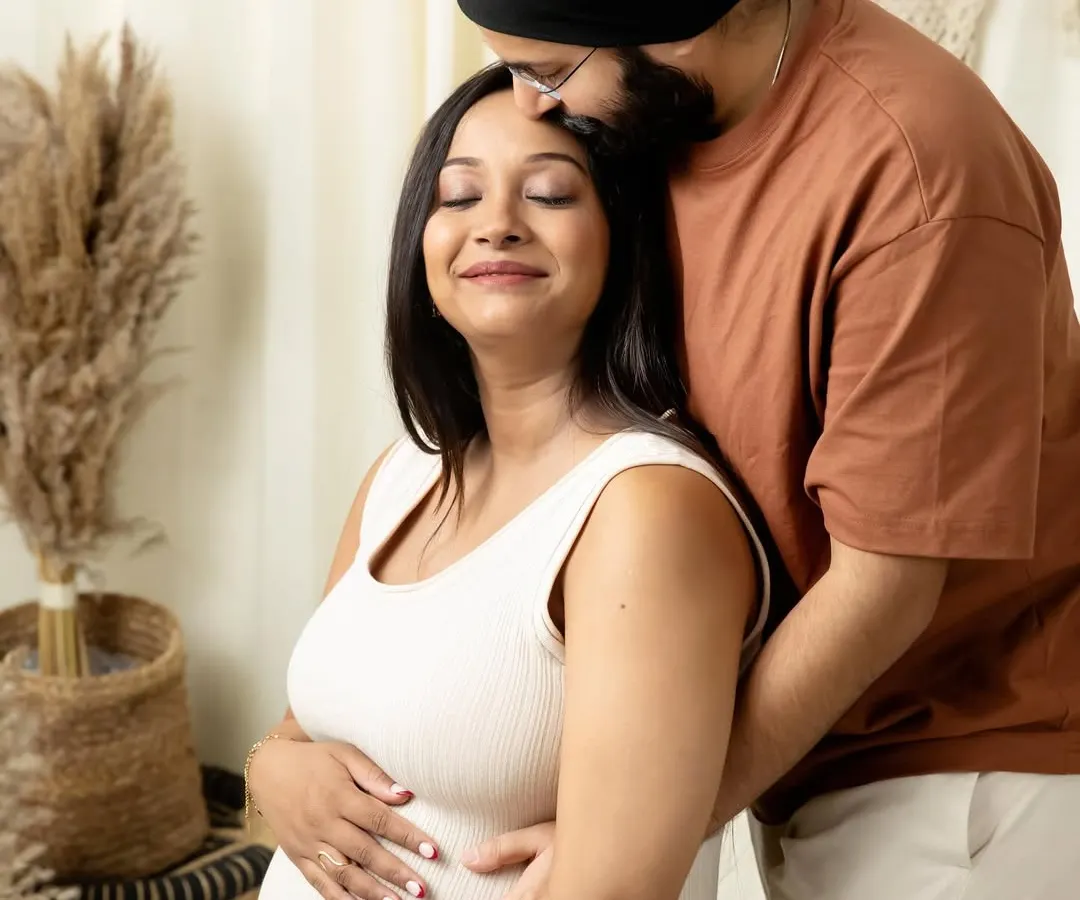 An intimate moment during a boho-themed studio maternity shoot, where an expecting father gently kisses his partner's forehead as she cradles her baby bump.