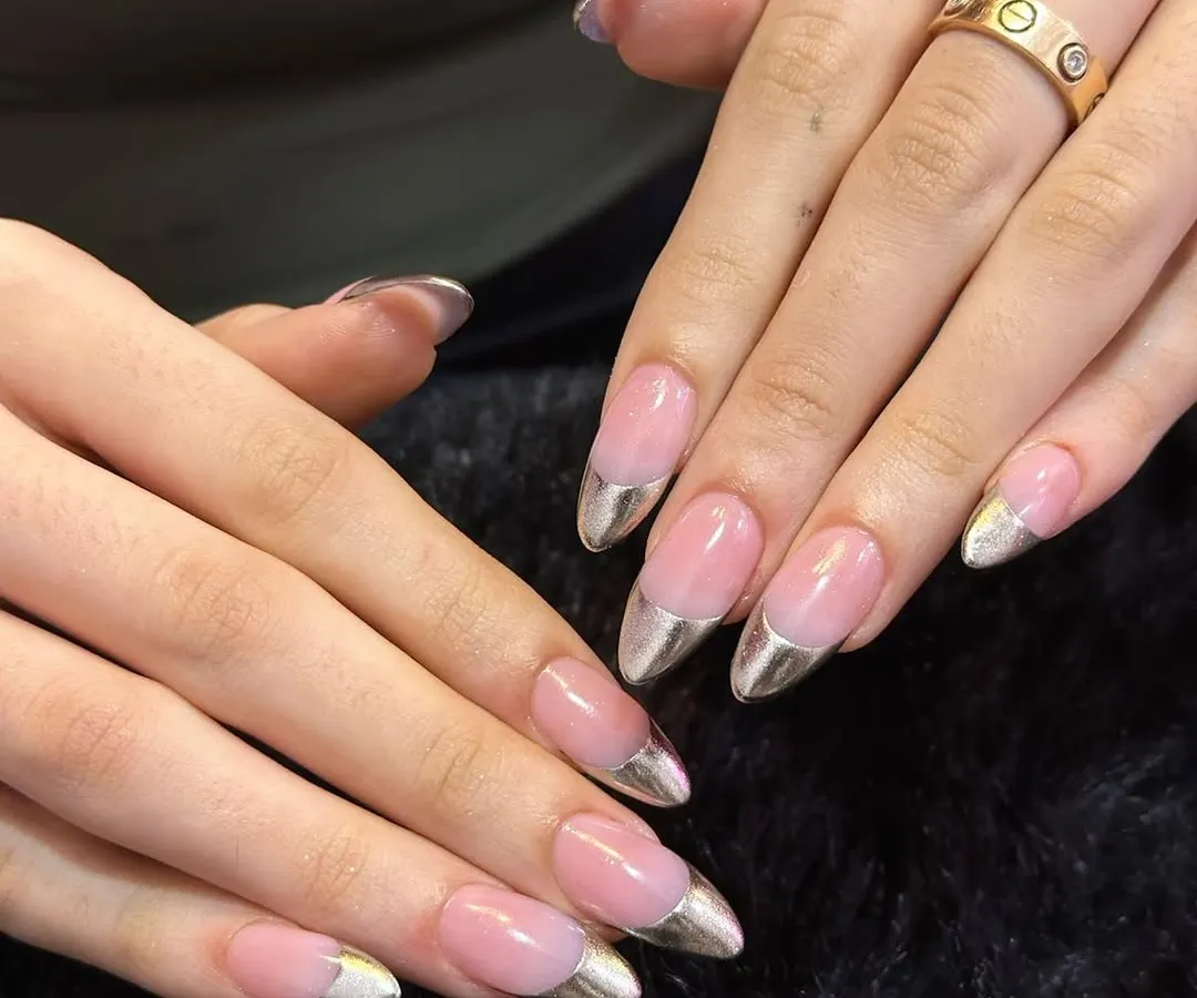 A modern classic. These nails feature a sharp, stiletto almond shape with a clean, natural pink base and futuristic liquid-metal silver chrome tips for a sleek and edgy French manicure.