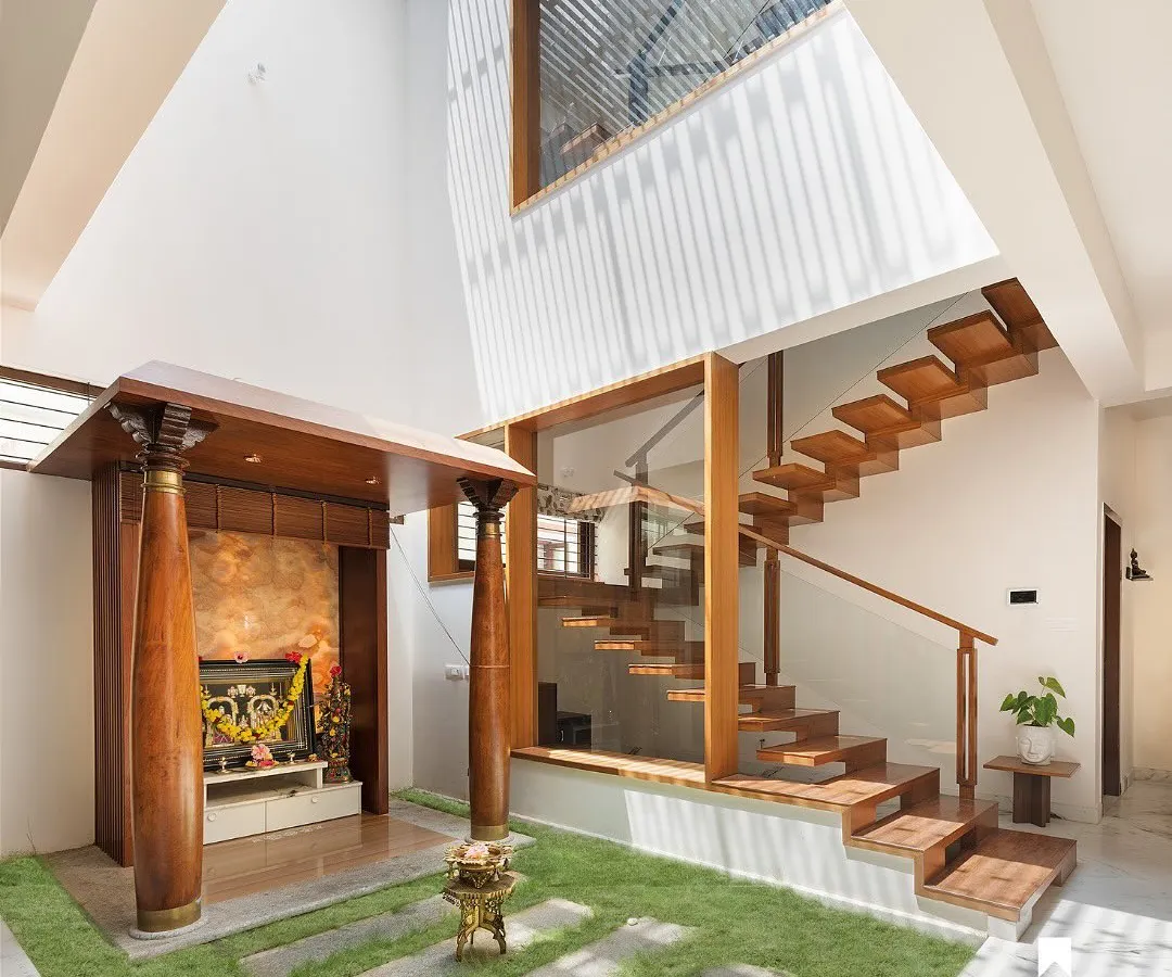 We believe every part of a home should be beautiful and functional. Here, a modern pooja room with traditional wooden pillars and a floating teak staircase coexist harmoniously, both illuminated by a double-height skylight that forms the spiritual and architectural heart of the home.