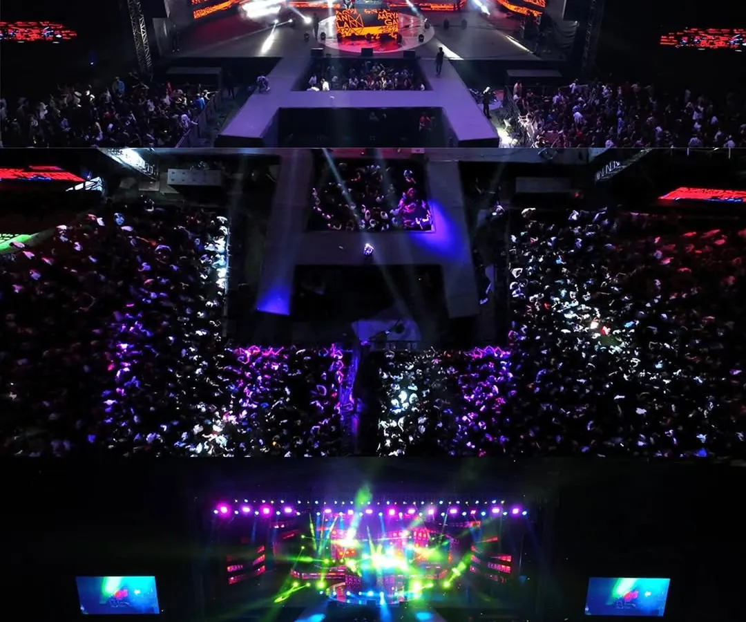 An aerial top-down shot capturing the immense crowd and spectacular stage lighting at Acharya Habba 2024. This perspective, only possible with professional drone videography, shows the sheer scale of the event and the energy of the audience.