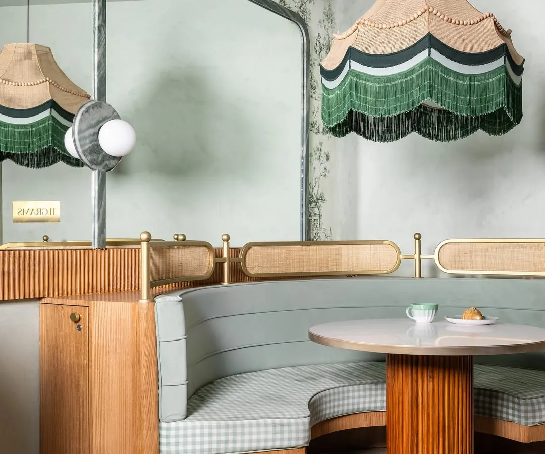 A detail from 11 Grams Cafe, this shot highlights our love for bespoke elements. The custom scalloped pendant lamp with green fringe hangs above a curved booth upholstered in gingham, creating a cozy nook that balances nostalgia with modern design.