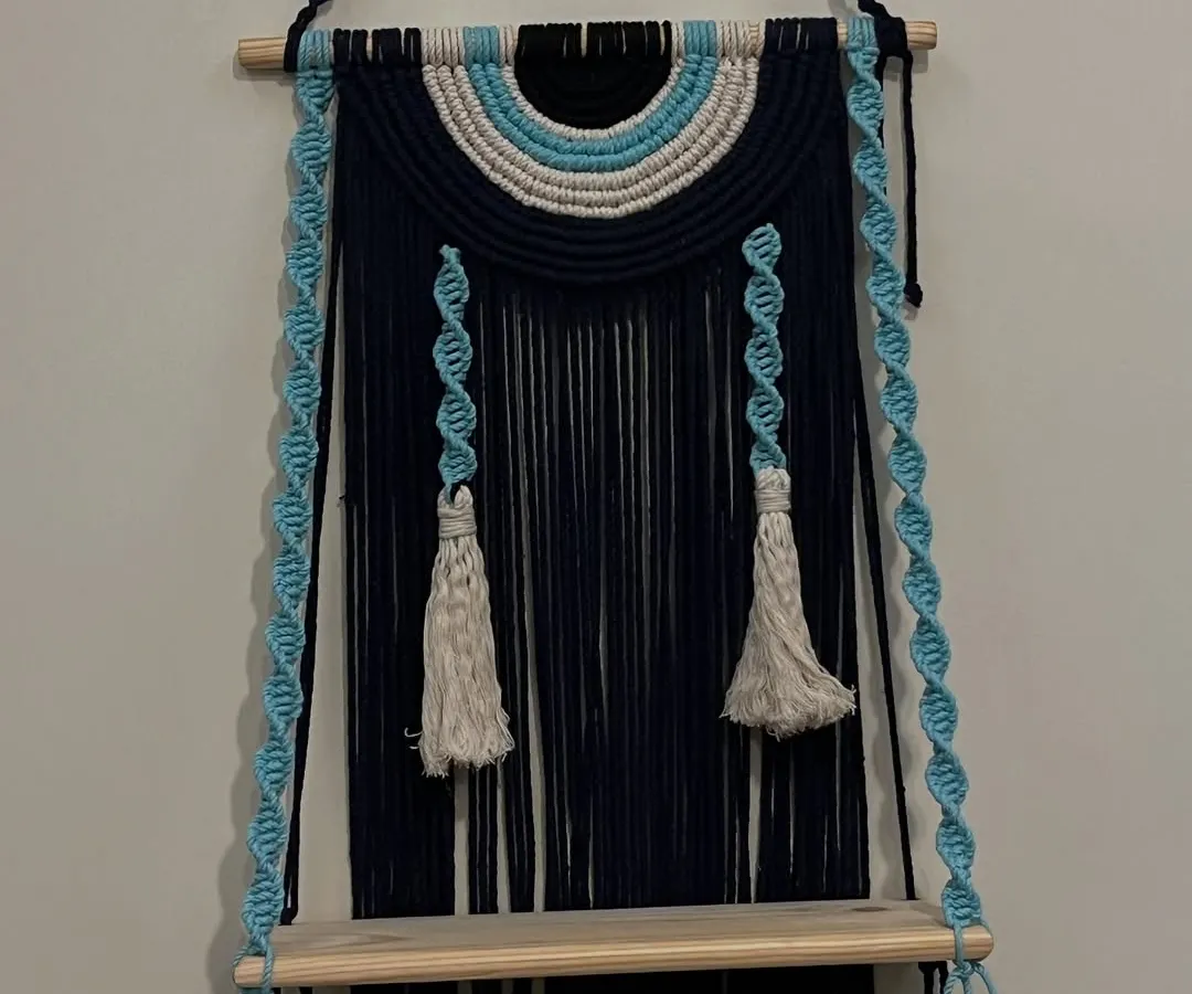 I love creating pieces that are both beautiful and useful. This evil eye themed wall shelf does just that, combining a protective symbol with a practical wooden shelf. The deep navy blue and sky blue cords with twisted hangers make it a unique piece to display small plants or treasures.