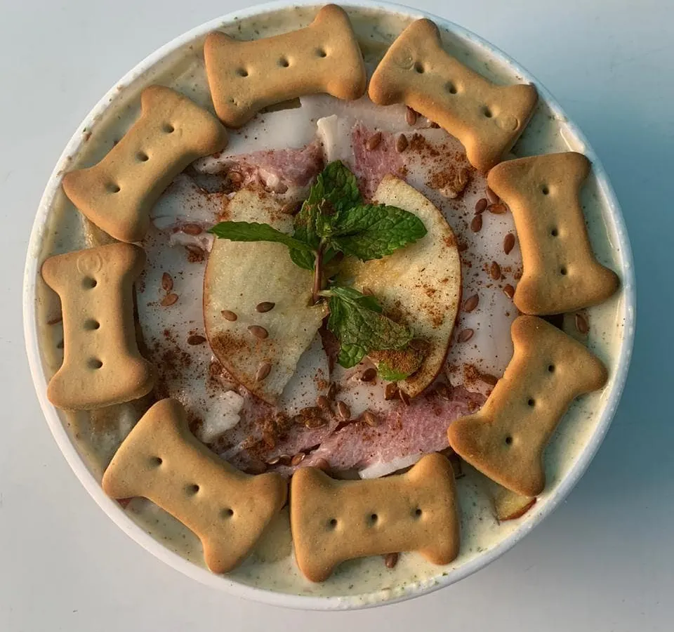 A close-up of my Apple & Bacon Pup Scoops. This dog-friendly ice cream is made with real ingredients, garnished with fresh apple, mint, and crunchy biscuits. It's a gourmet treat that's both delicious and healthy for your pup.