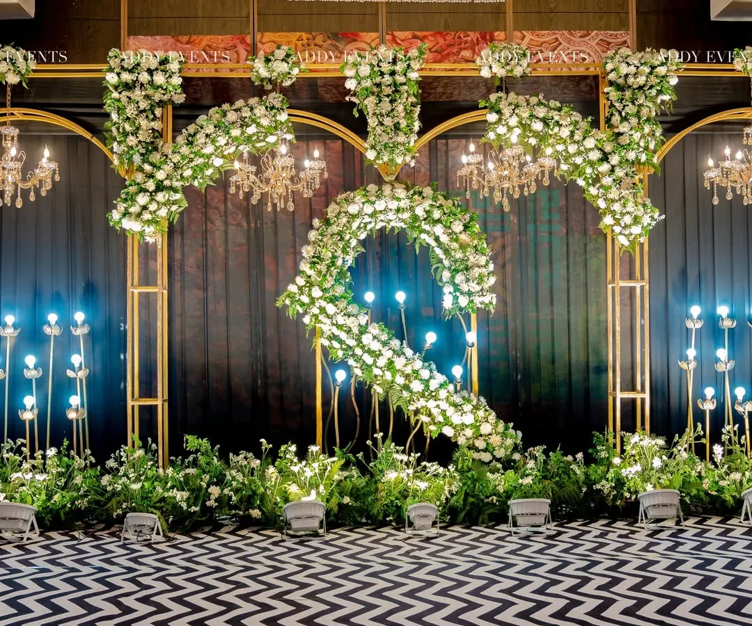 A bold statement for a modern Sangeet. This setup features a dramatic black and white chevron floor, custom floral monograms, and opulent chandeliers, proving that indoor ballroom events can be truly iconic.