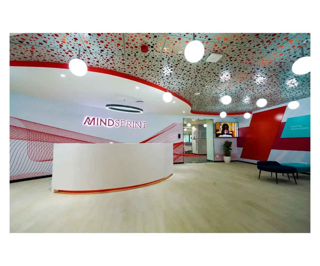 The reception for Mindsprint in Bangalore makes a bold first impression. We used a curved desk, intricate perforated ceiling with globe lighting, and the company's brand colors to create a welcoming yet futuristic entrance that immediately communicates a forward thinking identity.