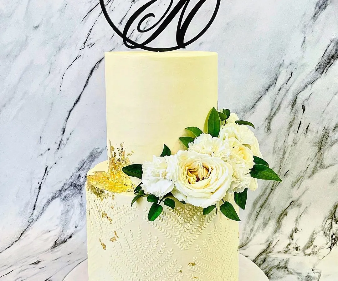 For a classic and romantic wedding, I created this elegant two-tier buttercream cake. The design features a subtle textured pattern on the bottom tier, touches of gold leaf, and a beautiful arrangement of fresh white roses and carnations, all topped with a custom "Y&N" monogram.