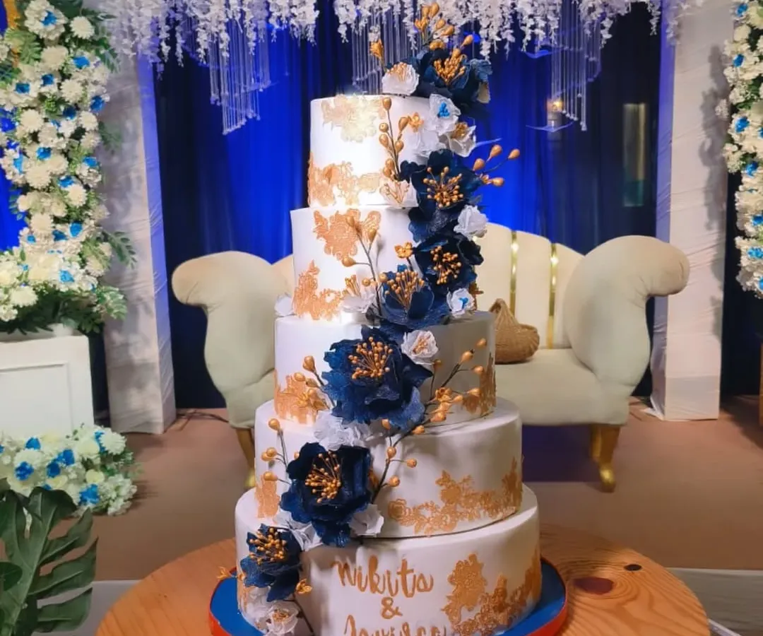 This is the biggest wedding cake I've made, weighing 25 kgs! It's a five-tier masterpiece with Dutch truffle and rum plum cake, decorated with handmade wafer paper peonies and delicate gold leaf accents.