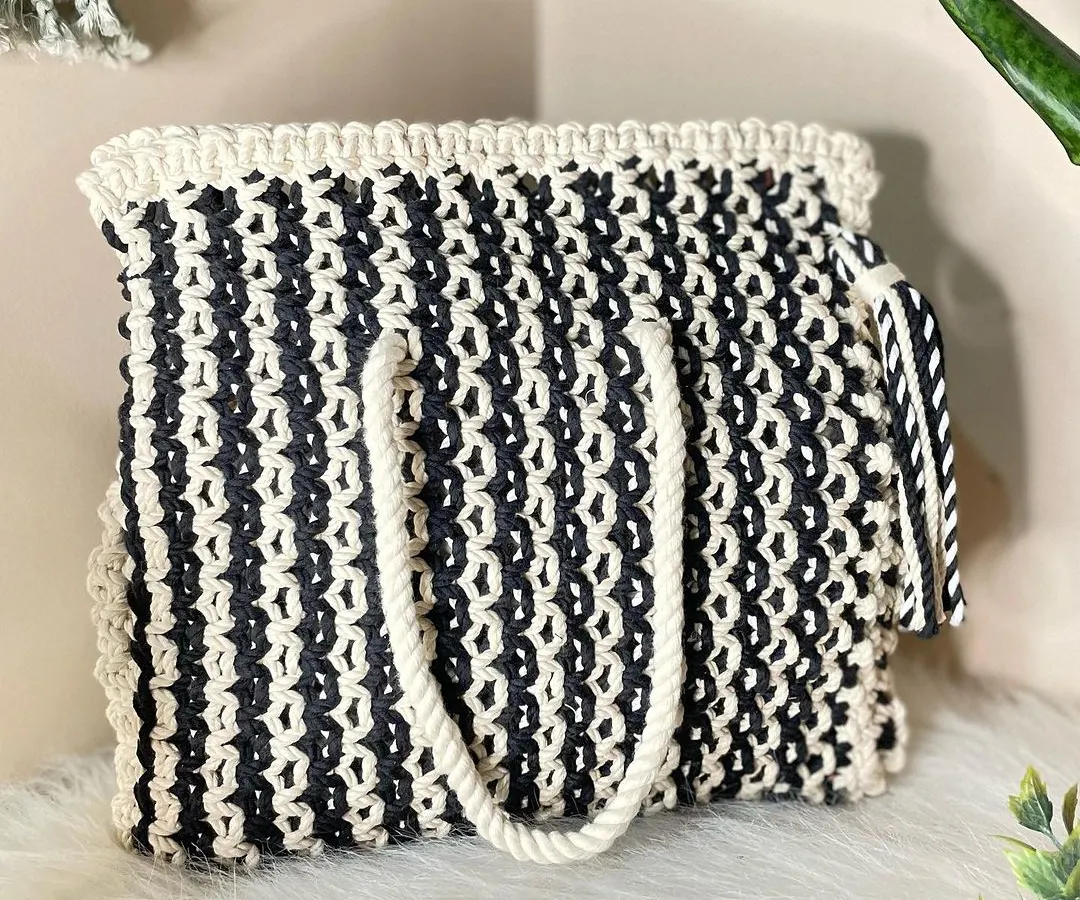 A classic that never goes out of style. This black and white macrame tote bag is spacious enough for all your essentials, featuring a thick, comfortable handle and a playful matching tassel.