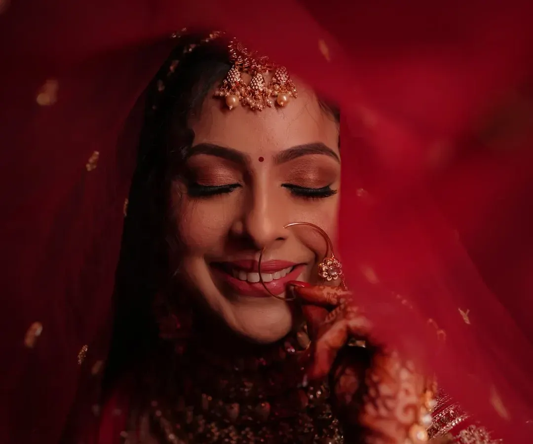 The quintessential blushing bride. This look focuses on a flawless, glowing base, soft smokey eyes, and a classic red lip, all framed by a delicate red veil for a timeless wedding day portrait.