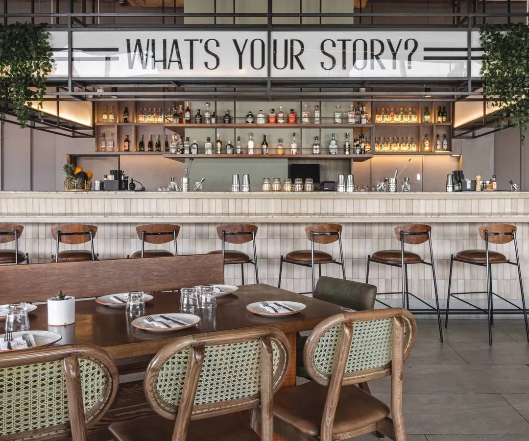 For Prequel, the bar is the heart of the space. We placed the brand's tagline, 'What's your story?', front and center to spark conversation, creating a focal point that is both a service area and a statement piece reflecting the restaurant's social, narrative driven identity.