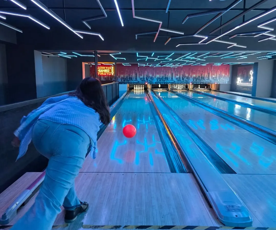 Feel the energy of our neon-lit bowling alley. This is a perfect wide-angle view of the action, showing a player about to release the ball down the glowing lane, ready for that satisfying strike.