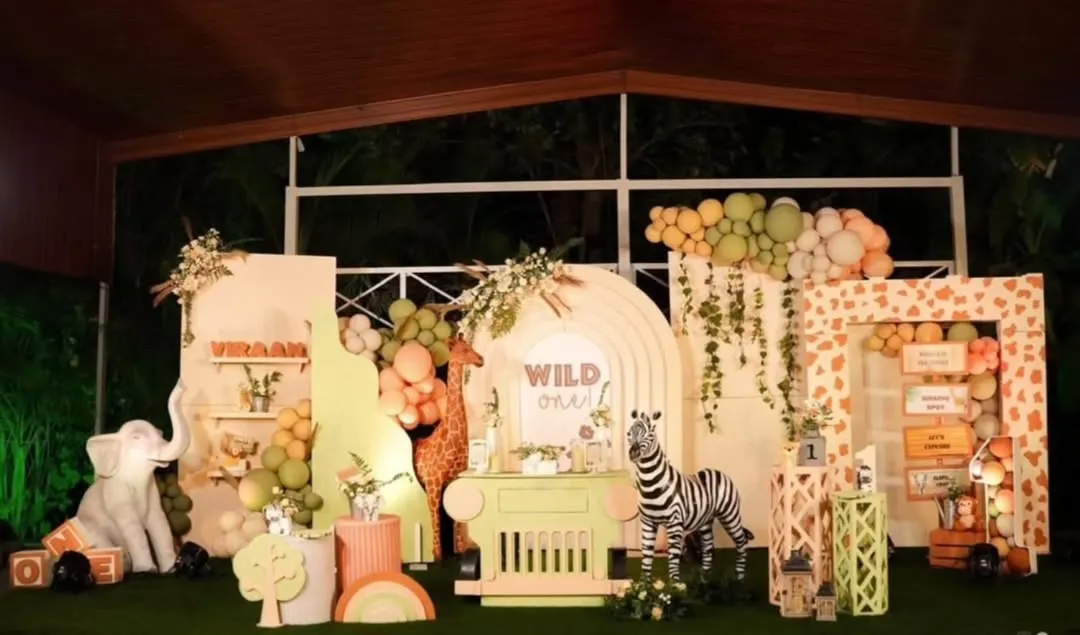 I bring the jungle to you with this "Wild One" safari-themed first birthday party. This expansive setup includes life-sized animal cutouts like a zebra and elephant, custom backdrops with giraffe prints, and lush green and earthy-toned balloon arrangements to create an immersive adventure for your little explorer.
