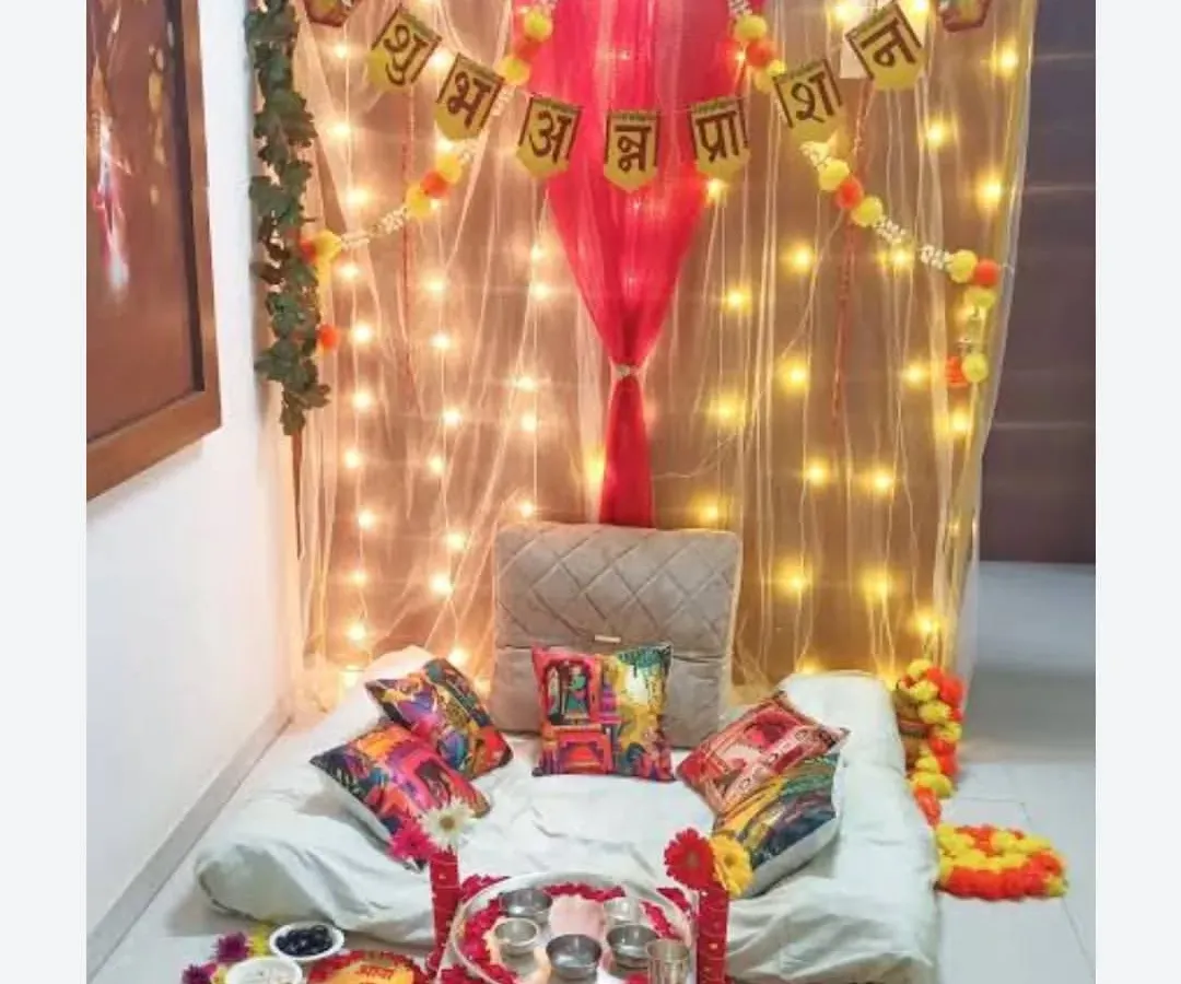 I create special, cozy setups for a baby's Annaprashan or first rice-eating ceremony. This design includes a soft, low seating area under a net canopy with twinkling lights, a 'Shubh Annaprashan' banner, and a traditional floral rangoli with spaces for all the ceremonial bowls.