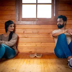 A relaxed portrait of a couple in a rustic, wood-paneled room. The warm lighting and casual poses create a feeling of comfort and easy companionship.
