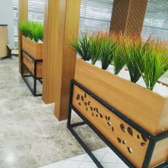 A close-up of the custom-designed planters for the restaurant. The warm wood box sits on a black metal frame with a decorative leaf-pattern cutout, adding a unique design detail that ties into the nature theme.