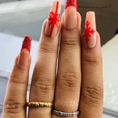 A creative Christmas design on long, coffin-shaped nails. This set features a red glitter French tip, a hand-painted bow to look like a gift, and a festive red snowflake.