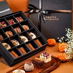 A closer look at our Malcha Box, featuring a curated selection of sixteen modern Indian sweet bites. This festive box includes unique treats like blueberry crumble tarts, pecan nut ladoos, and pistachio rose squares.