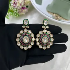 A close-up of the matching earrings for the kundan set, held to show the intricate meenakari detailing and the quality of the stones.