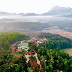 An aerial view of a resort in Sakleshpur, surrounded by misty hills and lush paddy fields. It's a hidden gem for a tranquil weekend getaway from Bangalore.
