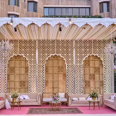 This stage was designed with a traditional jali backdrop, but softened with blush pink flooring, plush sofas, and elegant chandeliers for a modern royal look.