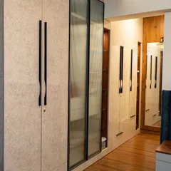 This wardrobe holds a clever secret. The design features a mix of textured laminate and fluted glass doors, with a small, custom-sized pouf tucked neatly into its own niche, ready to be pulled out for a comfortable seat.