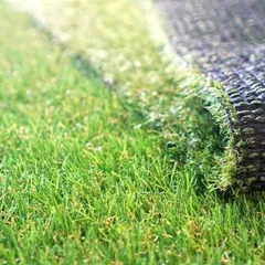 This macro shot highlights the realistic texture and color variation of the synthetic grass blades. The durable, perforated backing is also visible, which allows for proper drainage and long-term stability.