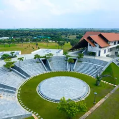 An aerial view of the large, open-air amphitheater at Vellore International School in Chennai. This space serves as the heart of the campus, a central node for school gatherings that is seamlessly integrated with the surrounding green landscape and waterbodies.