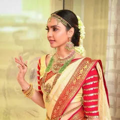A close-up of a South Indian bridal look. The focus is on defined eyes and flawless skin, complemented by traditional gold jewelry and a silk saree.