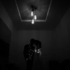 A romantic silhouette of the couple wrapped in fairy lights, their forms barely visible in the dark, creating an intimate and magical atmosphere.