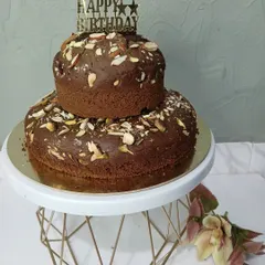 A simple yet delicious two-tier dry fruit cake for a birthday celebration. This cake is loaded with almonds and pistachios and topped with a 'Happy Birthday' sign, perfect for those who prefer less frosting.